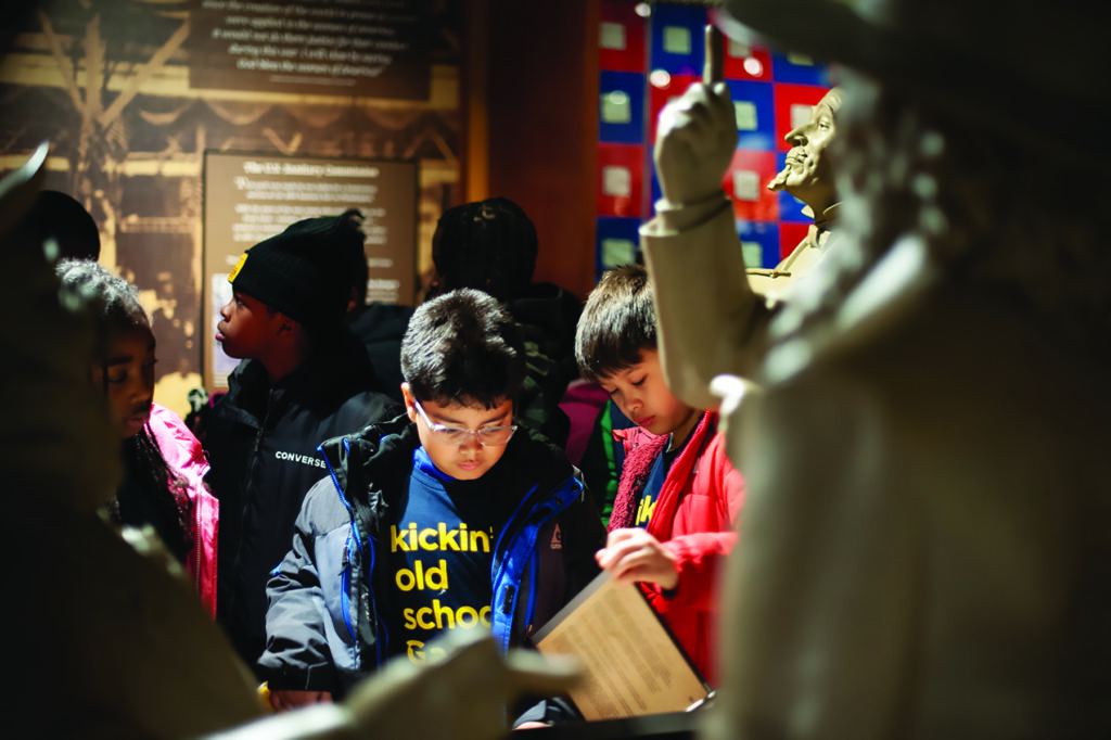 A group of young children stand in a museum and read a display.