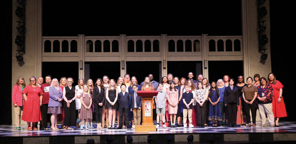 Picture of a group of adults and children standing on a stage and looking at the camera.