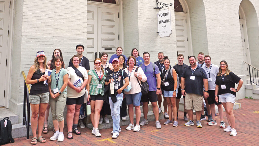 A group of people stand in front of a brick building with a hanging white sign reading "Ford's Theatre."